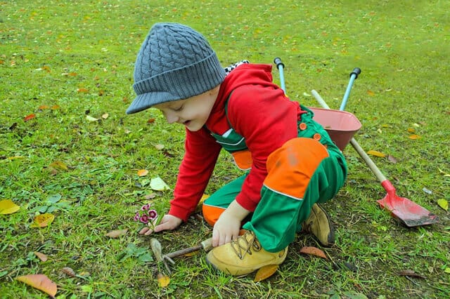 child holding gardening tool sitting on the ground